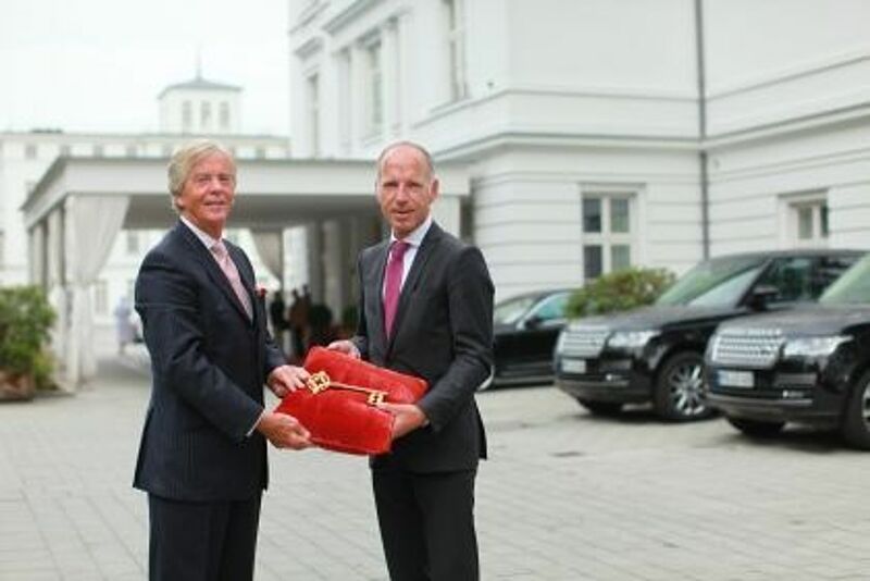 Peter J. Leitgeb (l.) händigt Tim Hansen, dem neuen Hoteldirektor des Grand Hotels Heiligendamm, symbolisch den Schlüssel für die Weiße Stadt am Meer aus.