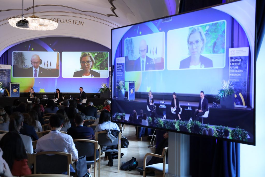 Saal mit vielen Menschen diese blicken auf große Leinwände mit Direktschaltungen