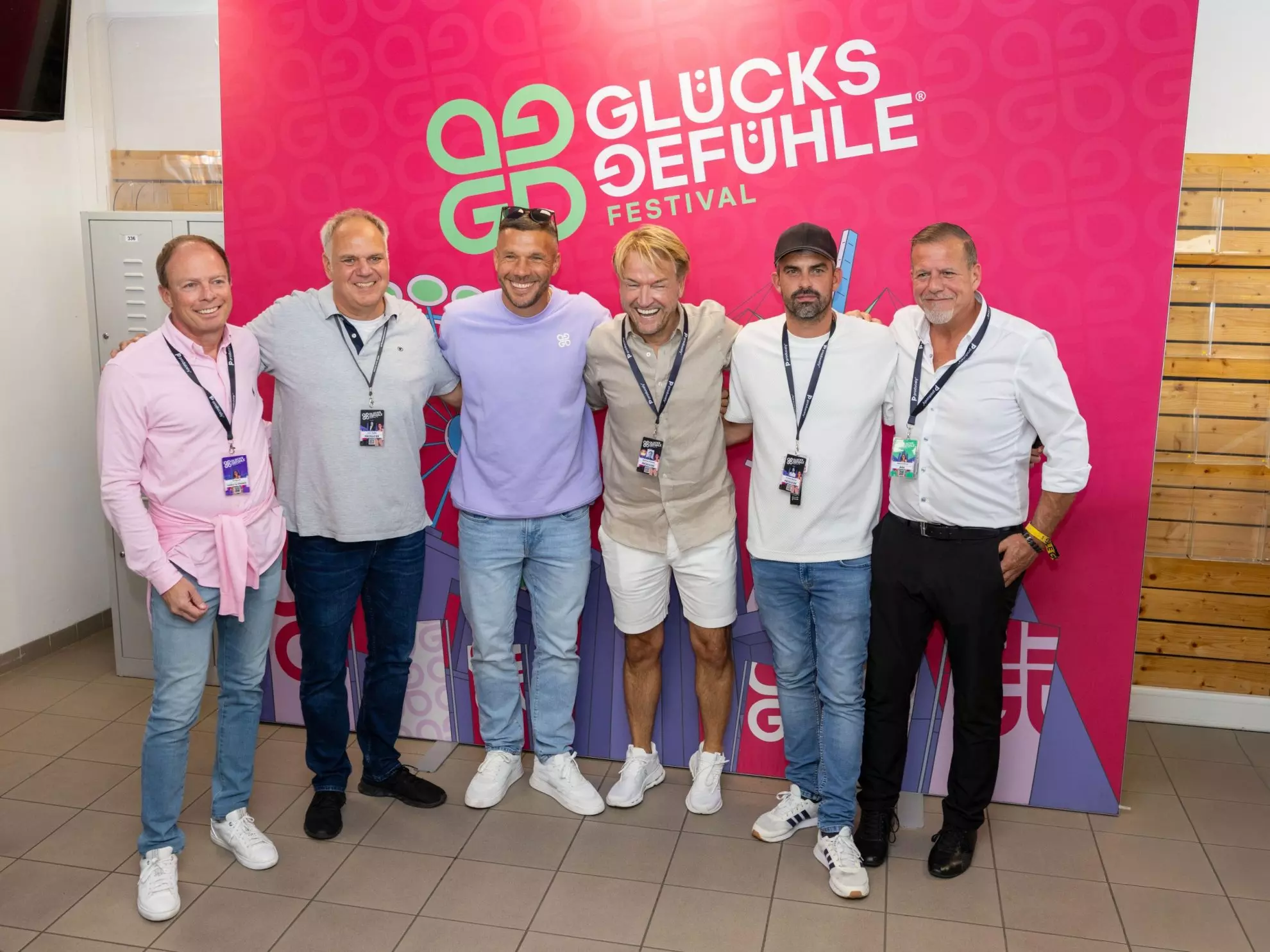 sechs lachende Männer vor Plakat mit Aufschrift Glückgefühle