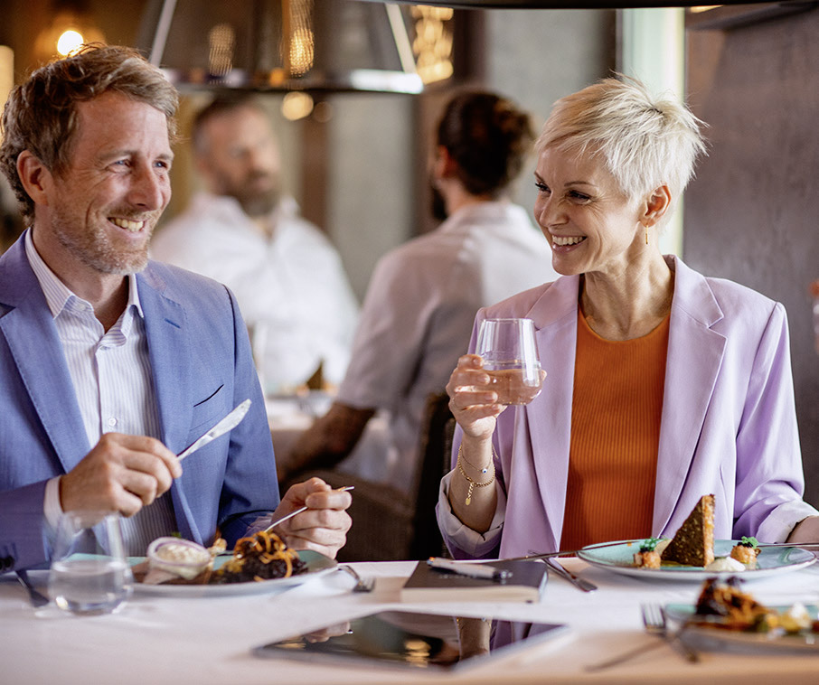 Man und Frau elegant gekleidet, sitzend am Tisch beim Essen