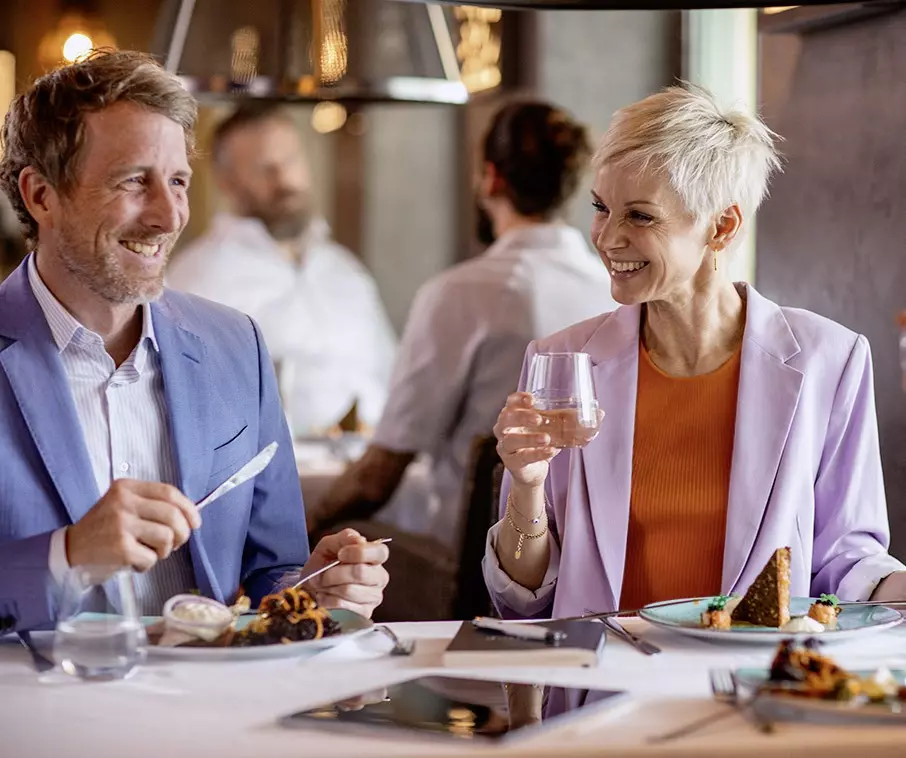 Man und Frau elegant gekleidet, sitzend am Tisch beim Essen