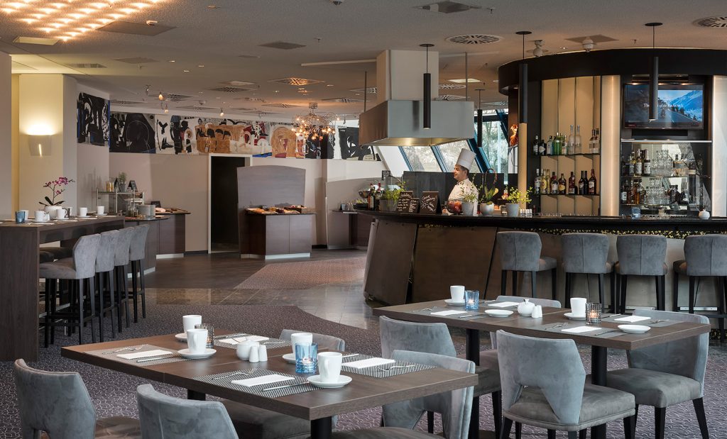 Frühstücksraum mit überwiegend grauer Bestuhlung und Theke