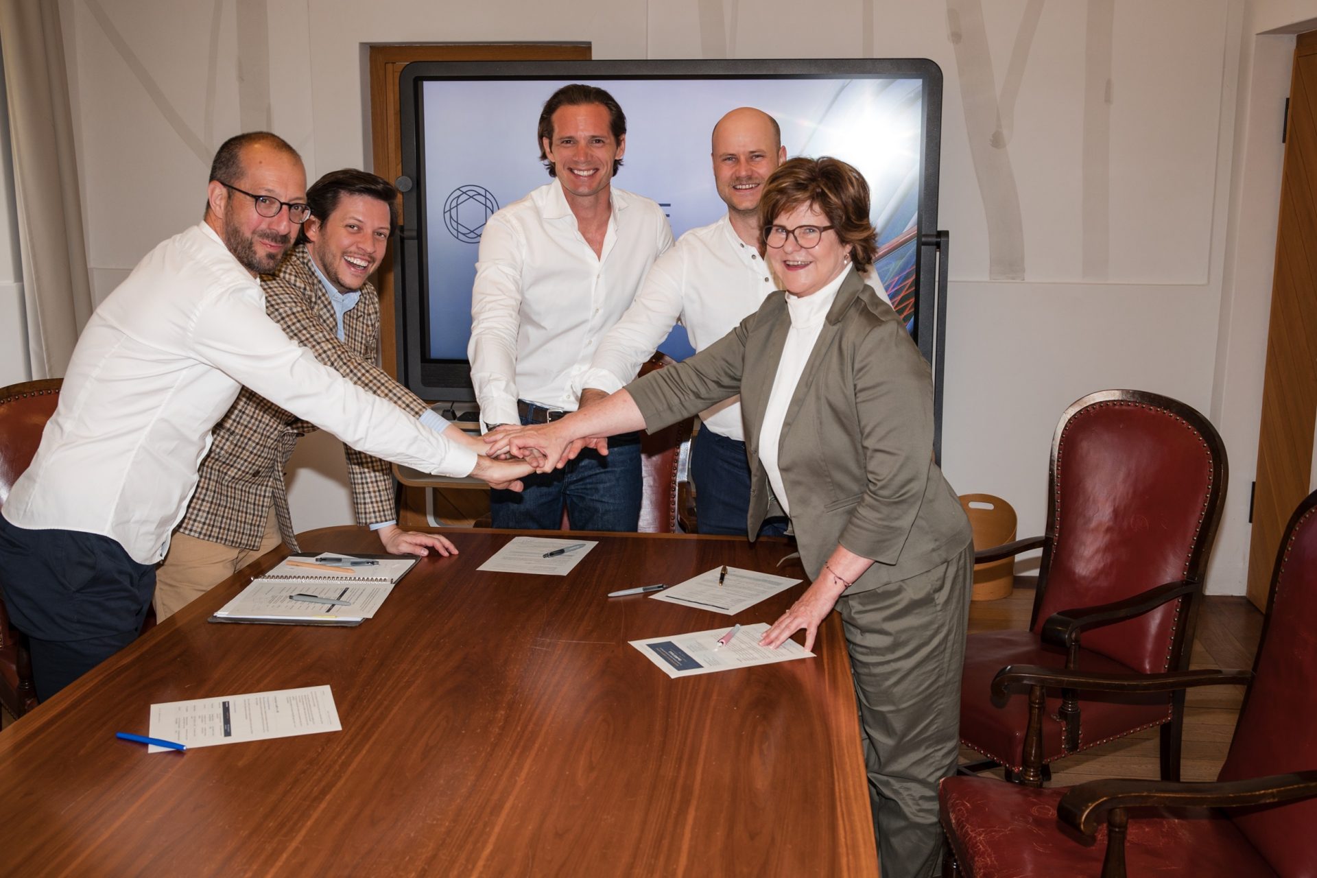 Gemeinsamer Auftakt für das Joint Venture OneMICE_Credit MICE Portal Fünf Personen besiegeln mit Handschlag und lächeln