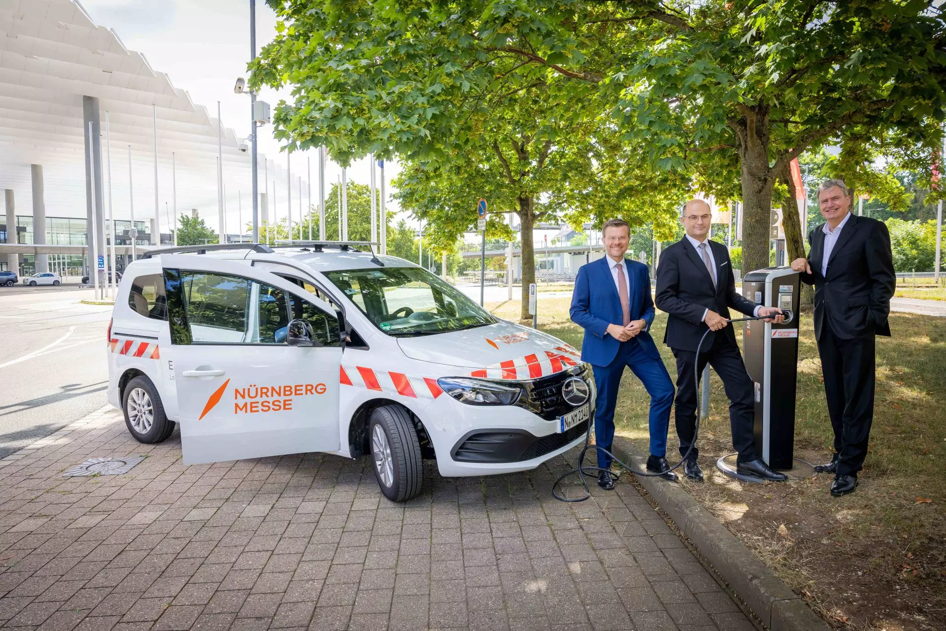 Auto vor E-Ladesäule mit 3 lächelnden Herren